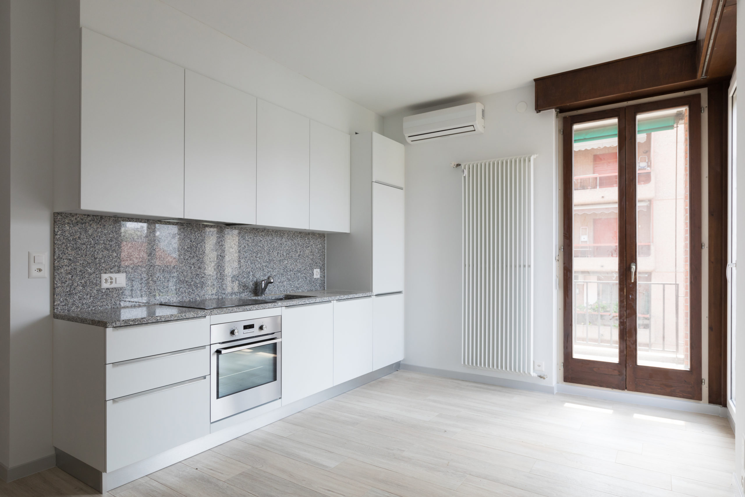 Large empty room with white walls and modern kitchen.